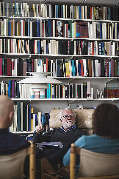 Senior therapist explaining couple while sitting against bookshelf