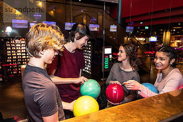 Cheerful multi-ethnic teenage friends standing with bowling balls