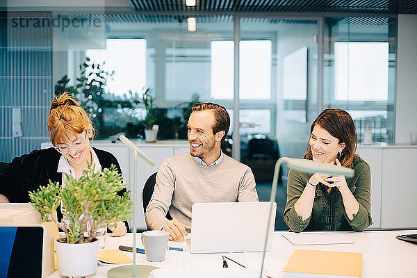 Cheerful business colleagues discussing while sitting at desk in creative office