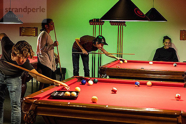 Teenagers playing pool on illuminated red tables
