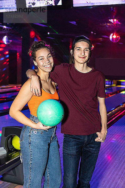 Portrait of smiling teenage friends standing with ball at bowling alley