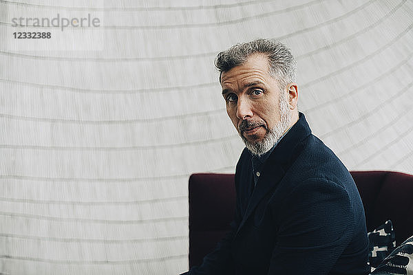 Portrait of mature businessman sitting on couch against wall at office