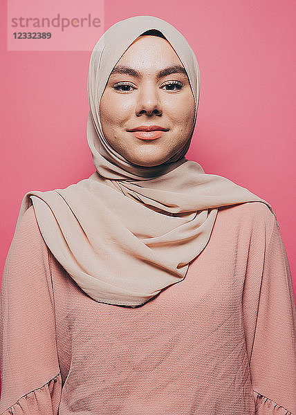 Portrait of smiling young woman wearing hijab against pink background