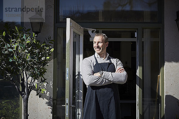 Confident mature owner looking away while standing with arms crossed outside store