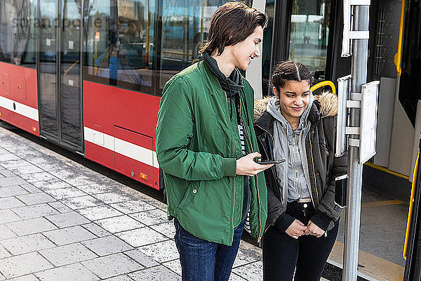 Smiling multi-ethnic teenagers standing on sidewalk against bus in city