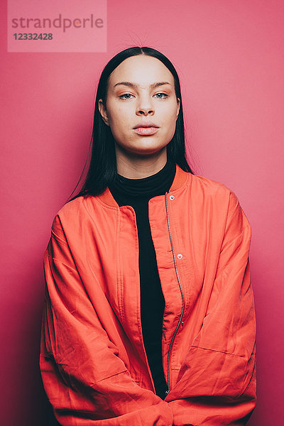 Portrait of confident woman wearing orange jacket over pink background