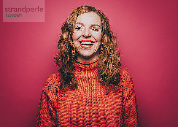 Portrait of smiling woman in orange top against pink background
