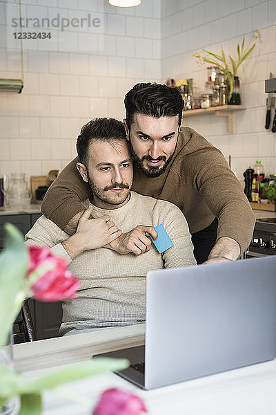 Homosexual couple doing online shopping through laptop in kitchen at home