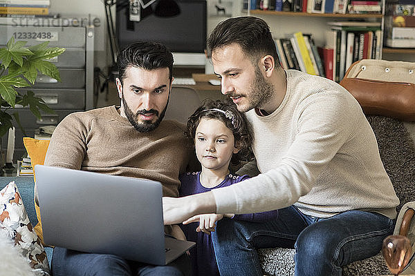Fathers showing laptop to daughter while sitting on chairs at home