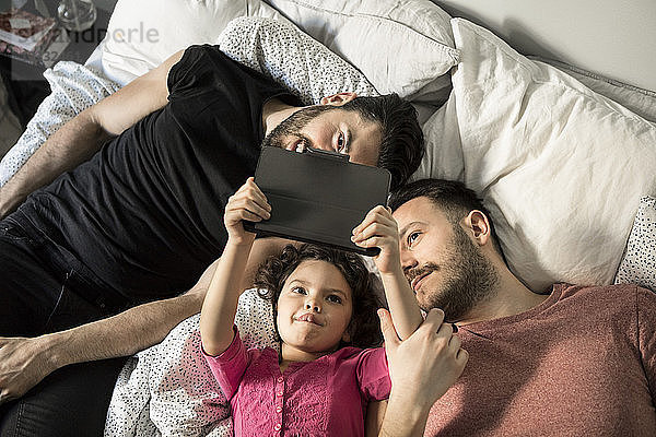 Daughter and fathers looking at digital tablet while lying on bed in bedroom