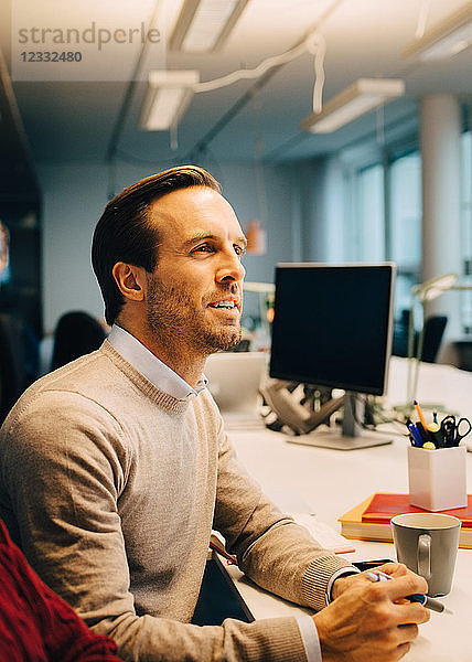 Confident businessman sitting at illuminated desk in creative office