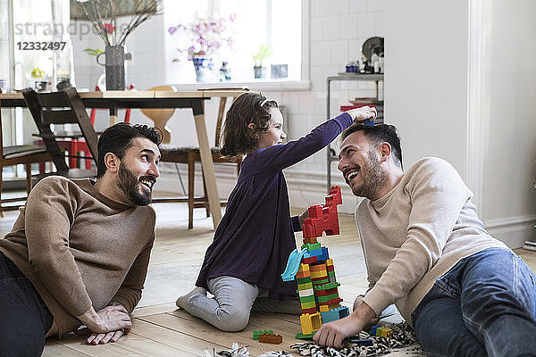 Cheerful fathers and daughter playing with toy blocks at home