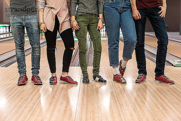 Low section of multi-ethnic friends standing on parquet floor at bowling alley