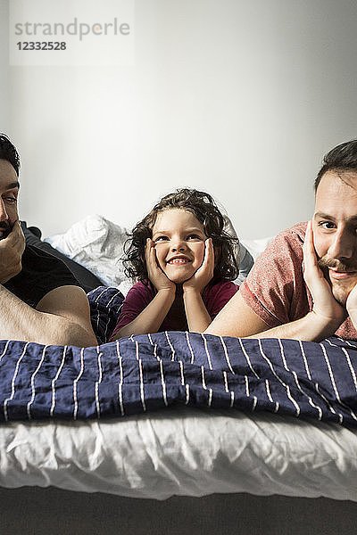 Fathers and daughter lying with head in hands on bed against wall