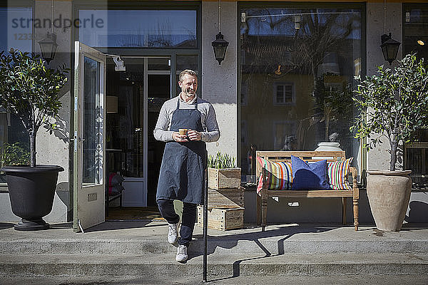 Full length of owner holding coffee mug while moving down from steps outside store