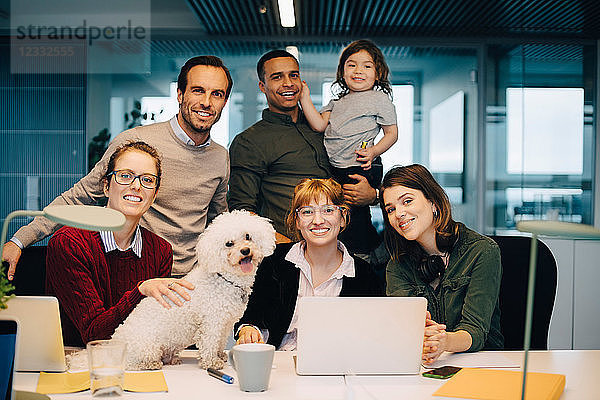 Portrait of smiling business team with kid and dog at creative office