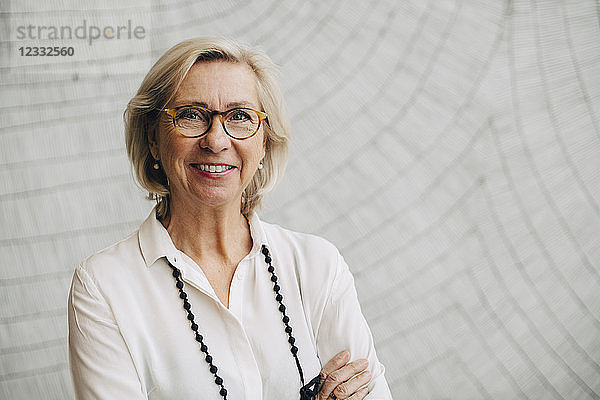Portrait of smiling senior businesswoman standing against wall in office