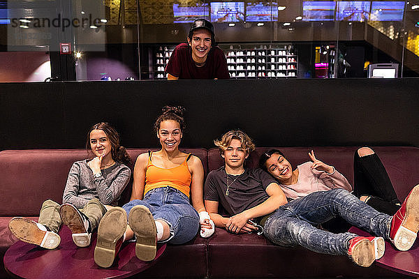 Portrait of happy multi-ethnic teenage friends on sofa at bowling alley