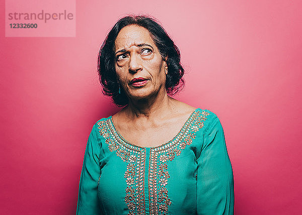 Thoughtful senior woman looking up against pink background