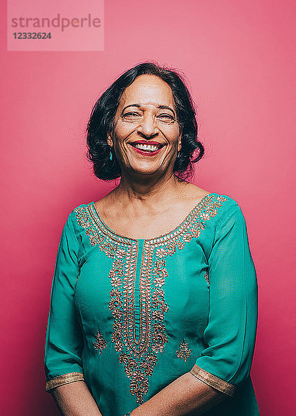 Portrait of smiling senior woman wearing salwar kameez on pink background