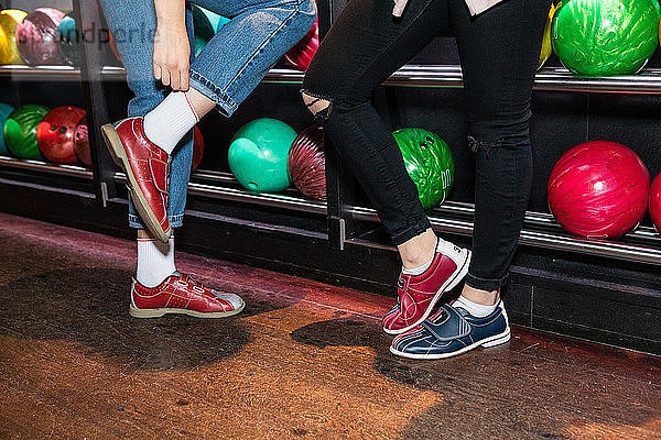 Low section of female friends wearing shoes standing by bowling rack