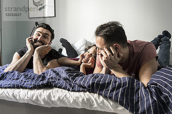 Cheerful fathers and daughter lying with head in hands on bed at home