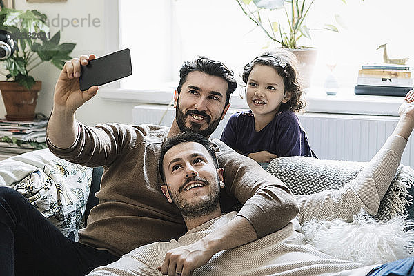 Fathers and daughter taking selfie through mobile phone in living room at home