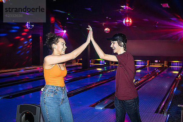 Cheerful friends giving high-five on illuminated parquet floor at bowling alley