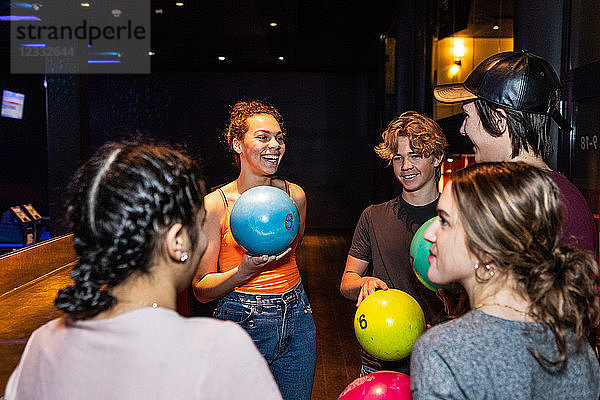Cheerful multi-ethnic teenagers talking while holding bowling balls