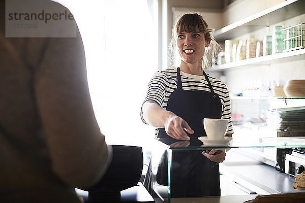 Smiling female barista serving coffee to male customer at cafe
