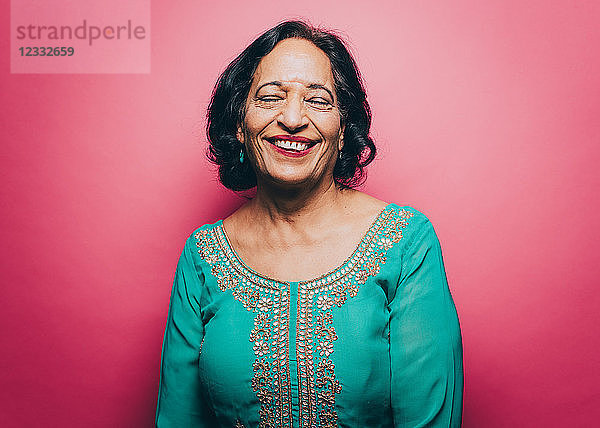 Smiling senior woman with eyes closed over pink background