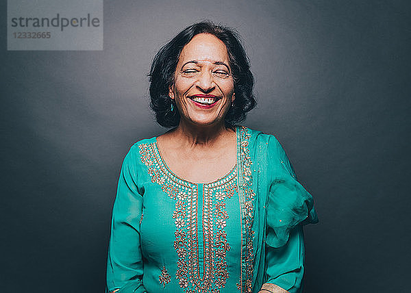 Smiling senior woman with eyes closed standing against gray background