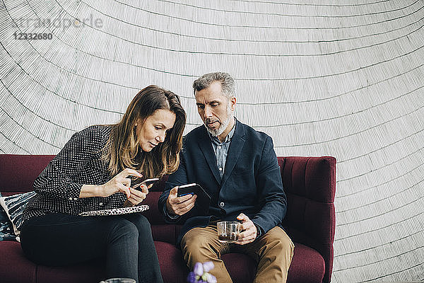 Businessman and woman using mobile phones while sitting on couch during conference