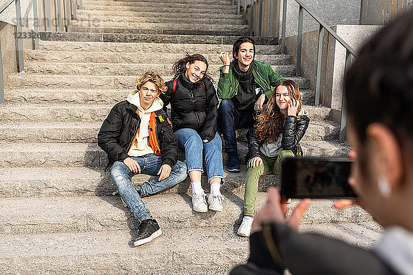 Cropped image of teenage girl photographing multi-ethnic friends sitting on steps in city
