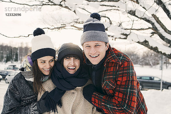 Cheerful friends in warm clothing embracing at park during winter