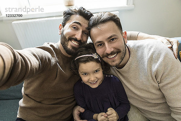 Smiling fathers and daughter taking selfie while sitting on sofa in living room at home