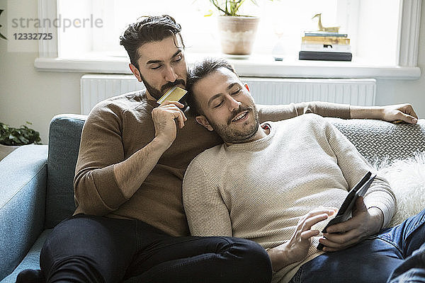 High angle view of homosexual couple doing online shopping while relaxing on sofa at home