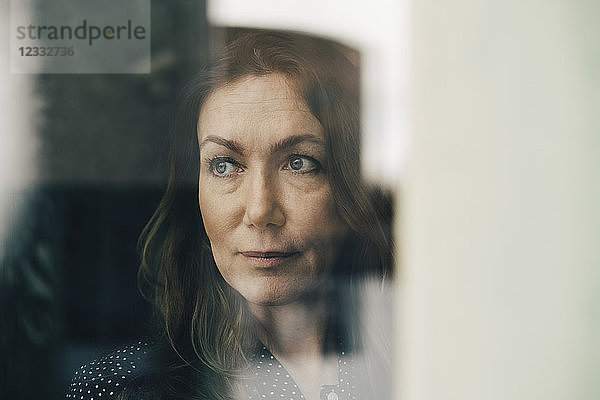 Close-up of mature businesswoman seen through window while looking away