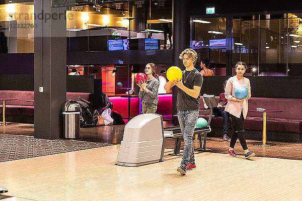 Multi-ethnic teenage friends playing with balls on parquet floor at bowling alley