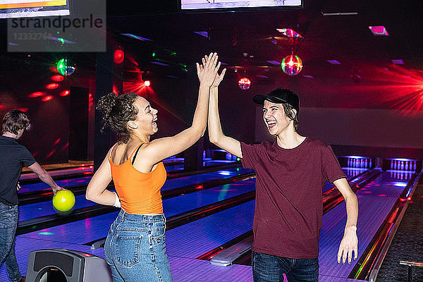 Cheerful friends giving high-five on parquet floor at bowling alley