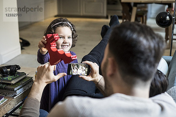 Smiling daughter showing red block to fathers resting in living room