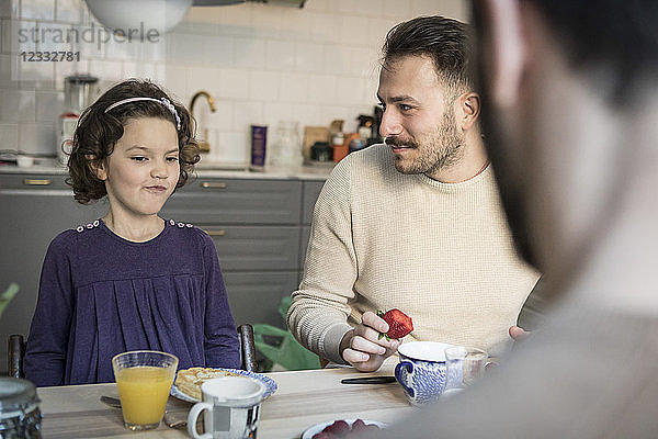 Father looking at daughter while having breakfast in kitchen