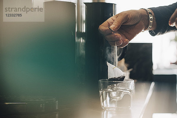 Cropped image of businesswoman making tea in drinking glass at office