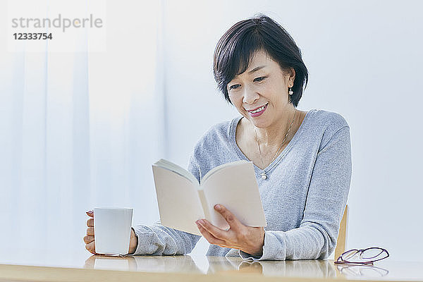Japanische ältere Frau  die am Tisch ein Buch liest
