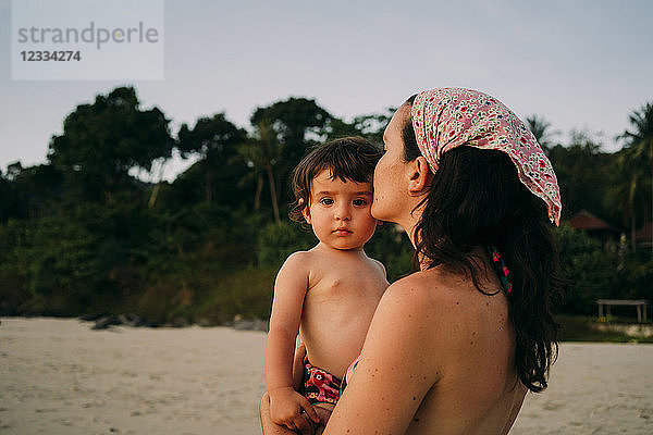 Mother holding and kissing her little daughter on the beach by sunset