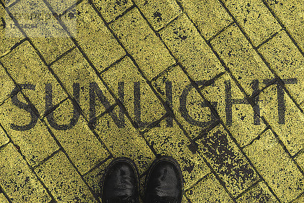 Black shoes on yellow pavement with stenciled word 'Sunlight'