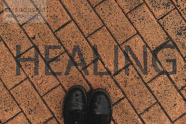 Black shoes on orange pavement with stenciled word 'Healing'