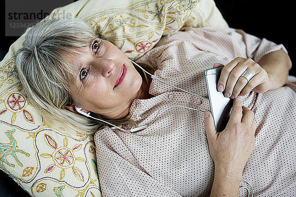Smiling mature woman lying down with cell phone and earphones
