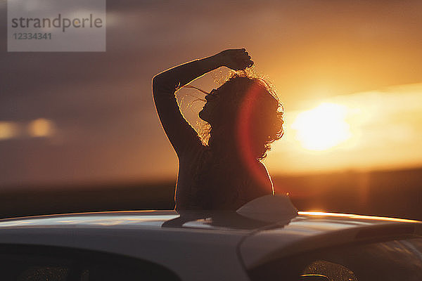 Woman outside the car at sunset  raised arm
