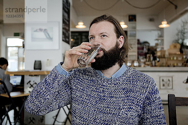 Man with beard sitting in cafe  drinking water